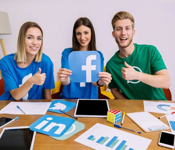 smiling-woman-holding-facebook-logo-with-his-friends-showing-thumbup-sign (1)